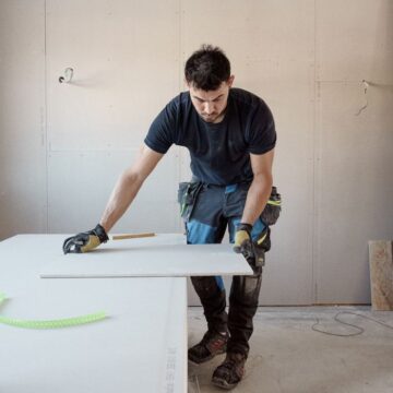 A blue collar worker measuring a plank indoors in a bright workshop.