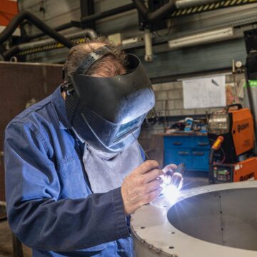 A skilled welder working in a modern workshop with advanced equipment and safety gear.