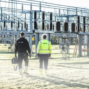 Two workers inspect an outdoor electrical substation, emphasizing safety and maintenance.