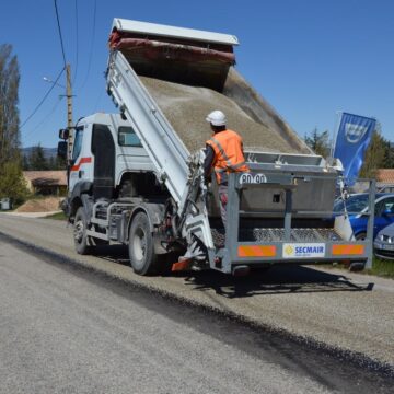 A dump truck unloading asphalt during road work with a worker in a reflective jacket.