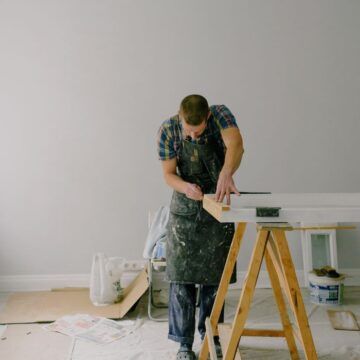 Full length of skilled craftsman in dirty apron repairing and restoration wooden window in light room